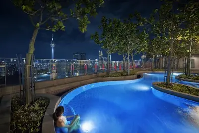 a man sitting in a chair next to a swimming pool at night at S20- Bedroom Bukit Bintang Robertson with Netflix in Kuala Lumpur