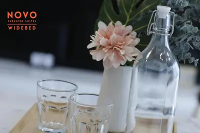 two glasses and a bottle and a vase with a flower at NOVO Serviced Suites by Widebed, Jalan Ampang, Gleneagles in Kuala Lumpur