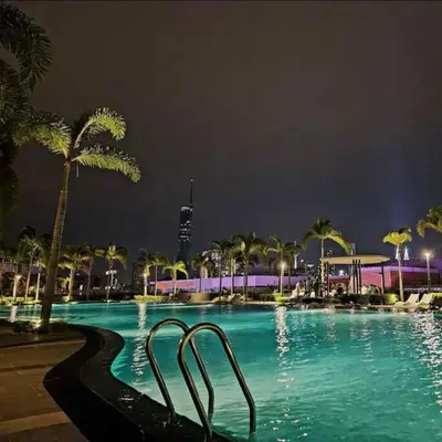a swimming pool at night with palm trees and a building at Chill-houz KL Trion 6P 2BR - 5-mins MRT - TRX Mall in Kuala Lumpur