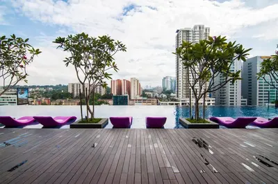 a rooftop pool with purple chairs and trees and a city at Nadi Bangsar by Plush in Kuala Lumpur