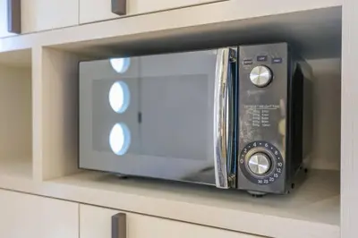 a microwave oven on a shelf in a cabinet at KL Sanctuary Style Comforts, Pool, Gym, Near MRT! in Kuala Lumpur
