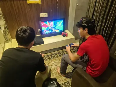 two men playing a video game in front of a television at Infinity View KL Hostel in Kuala Lumpur