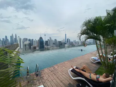 a woman laying in chairs by a pool with a city skyline at Celestial Heights Hostel featuring Infinity Skypool in Kuala Lumpur