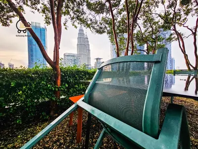 a green chair in a park with a city skyline at The Mews KLCC by GBS in Kuala Lumpur