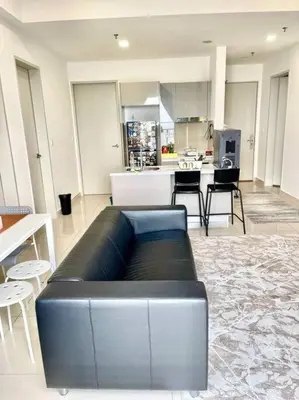 a living room with a black couch and a kitchen at Trion Kuala Lumpur KLCC view L65 2br 2bth in Kuala Lumpur