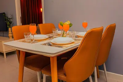 a dining room table with orange chairs and a table with glasses at The Atrium at Jalan Ampang by OKBnB - Cozy 2 Bedroom, 3 mins to KLCC in Kuala Lumpur