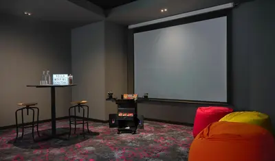 a room with a large screen and a table and chairs at Moxy Kuala Lumpur Chinatown in Kuala Lumpur