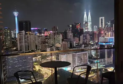 a view of a city at night with a table and chairs at The BirdsEye View facing KLCC with Gorgeous pools in Kuala Lumpur