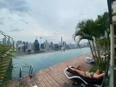 two people laying on lounge chairs next to a swimming pool at Elevated Horizons Hostel & Infinity Suites Skypool in Kuala Lumpur
