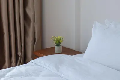 a bed with white sheets and a vase of flowers on a table at Bintang Goldhill, 5M to TRX in Kuala Lumpur