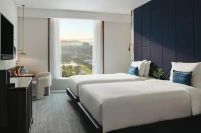 two beds in a hotel room with a large window at Kimpton Naluria Kuala Lumpur by IHG in Kuala Lumpur
