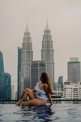a woman sitting in a infinity pool with a city skyline at The Luxe & Colony KLCC By LuxeHub in Kuala Lumpur