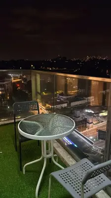 a table and chairs on top of a balcony at night at Infinity Sky Pool, Regalia Suite KLCC in Kuala Lumpur