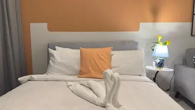 a bed with white sheets and an orange wall at KLCC view couple stay 276A at KLCC in Kuala Lumpur
