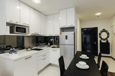 a kitchen with white cabinets and a table and a refrigerator at Mercu Summer Suites Bernice KLCC in Kuala Lumpur