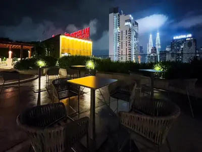 a rooftop bar with tables and chairs at night at Majestic Residence Infinity Pool with KLCC View in Kuala Lumpur