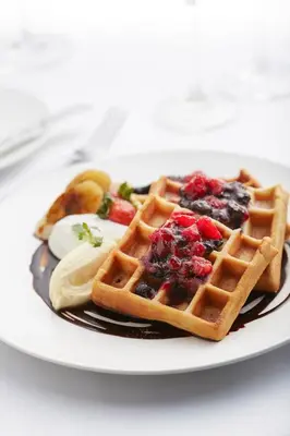 a plate of waffles with berries and butter on it at THE FACE Suites Hotel in Kuala Lumpur