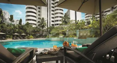 a pool with chairs and a table with drinks and an umbrella at Shangri-La Kuala Lumpur in Kuala Lumpur