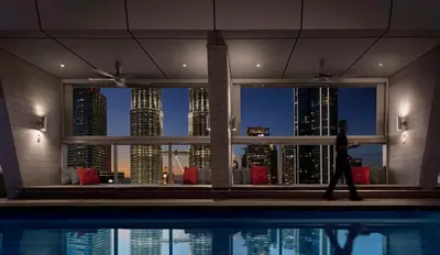 a woman walking by a swimming pool in front of a city skyline at Traders Hotel, Kuala Lumpur in Kuala Lumpur