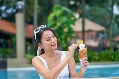 a woman holding an ice cream cone in a pool at Le Méridien Kuala Lumpur in Kuala Lumpur