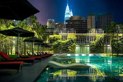 a pool with chairs and umbrellas and a city at night at E&O Residences Kuala Lumpur in Kuala Lumpur