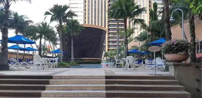a pool with white chairs and blue umbrellas and palm trees at Better Residence Suite at Times Square Bukit bintang kl in Kuala Lumpur