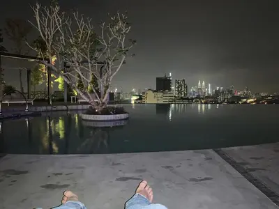 a person sitting on the edge of a pool at night at 2 bedroom apartment at 28 Boulavard in Kuala Lumpur