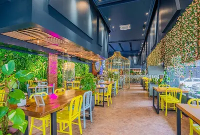 a restaurant with tables and yellow chairs and plants at Hotel Olympic Malaysia Kuala Lumpur in Kuala Lumpur