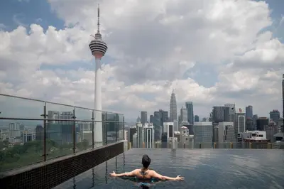 a man in a infinity pool with a view of the city at Ceylonz Suites KLCC Rooftop Infinity Pool KL Tower View in Kuala Lumpur