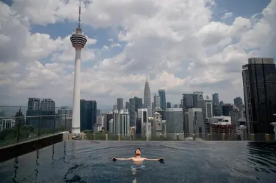 a woman swimming in a pool on top of a skyscraper at Ceylonz Suites KLCC Rooftop Infinity Pool KL Tower View in Kuala Lumpur