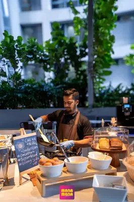 a man in an apron preparing food on a table at Ceylonz Suites KLCC Rooftop Infinity Pool KL Tower View in Kuala Lumpur