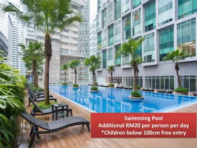 a swimming pool with chairs and palm trees in front of a building at Soho Suites KLCC by GuestHouse in Kuala Lumpur