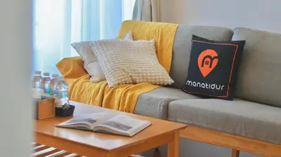 a couch with a pillow and a table with a book at UNA Serviced Apartment by manatidur in Kuala Lumpur