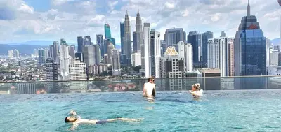 two people swimming in the infinity pool on the roof of a skyscraper at Regalia Suites KLCC View Rooftop Infinity Pool by SHI in Kuala Lumpur