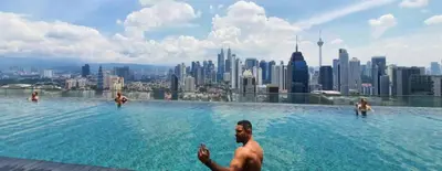 a man sitting in a swimming pool with a city skyline at Regalia Suites KLCC View Rooftop Infinity Pool by SHI in Kuala Lumpur