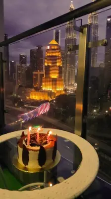 a cake with candles on a table in front of a window at KLCC VIEW-3 BED LOVELY APARTMENTS IN KUALA LUMPUR in Kuala Lumpur