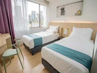 a bedroom with two beds and a chair and a window at Floresta Hotel Chinatown in Kuala Lumpur