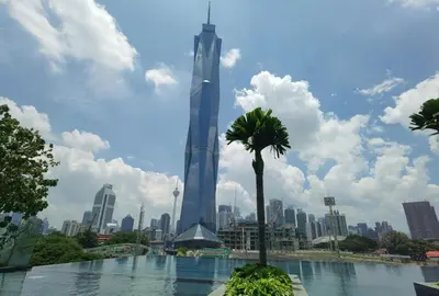 a tall building with a palm tree in front of a city at Opus Residences KL 118 View in Kuala Lumpur