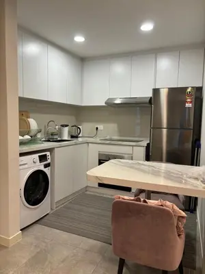 a kitchen with white cabinets and a table and a dishwasher at The Ooak Suites by Bamboo Hospitality in Kuala Lumpur